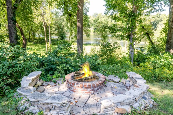 A stone fire pit surrounded by rocks and greenery in a forested area.