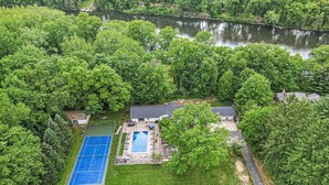 Ett flygbildsfoto av en fastighet med en swimmingpool, en tennisbana och en flod.