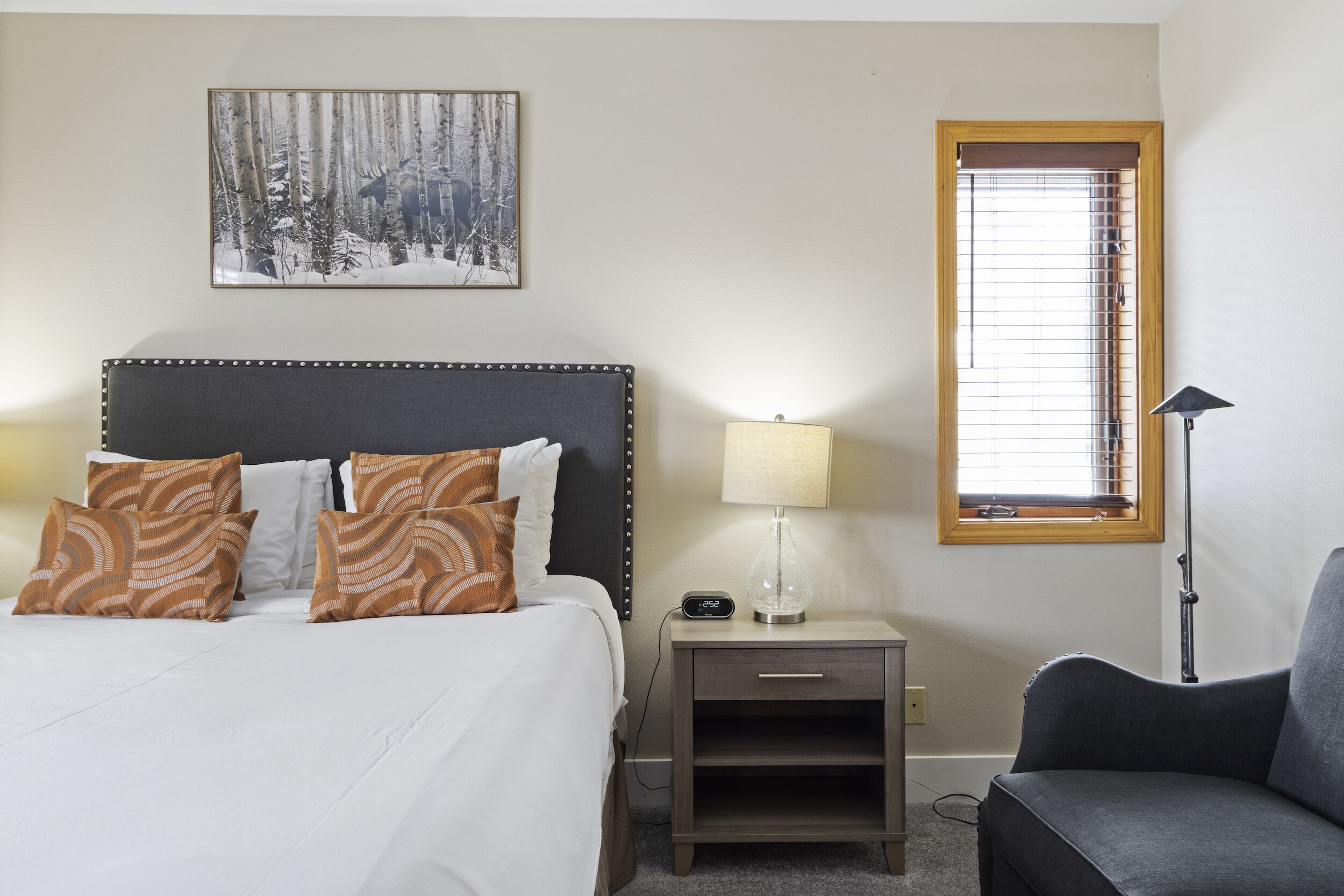 A neatly arranged bedroom with a bed, bedside table, lamp, and a chair.