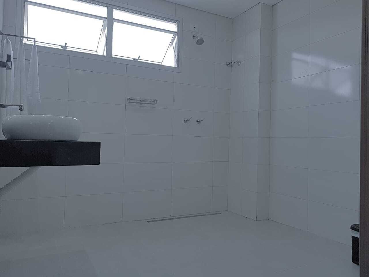 A bathroom with white tiles, a window, a sink, and a shower.