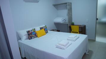 A hotel room with a bed, pillows, a towel rack, a desk, and a chair.