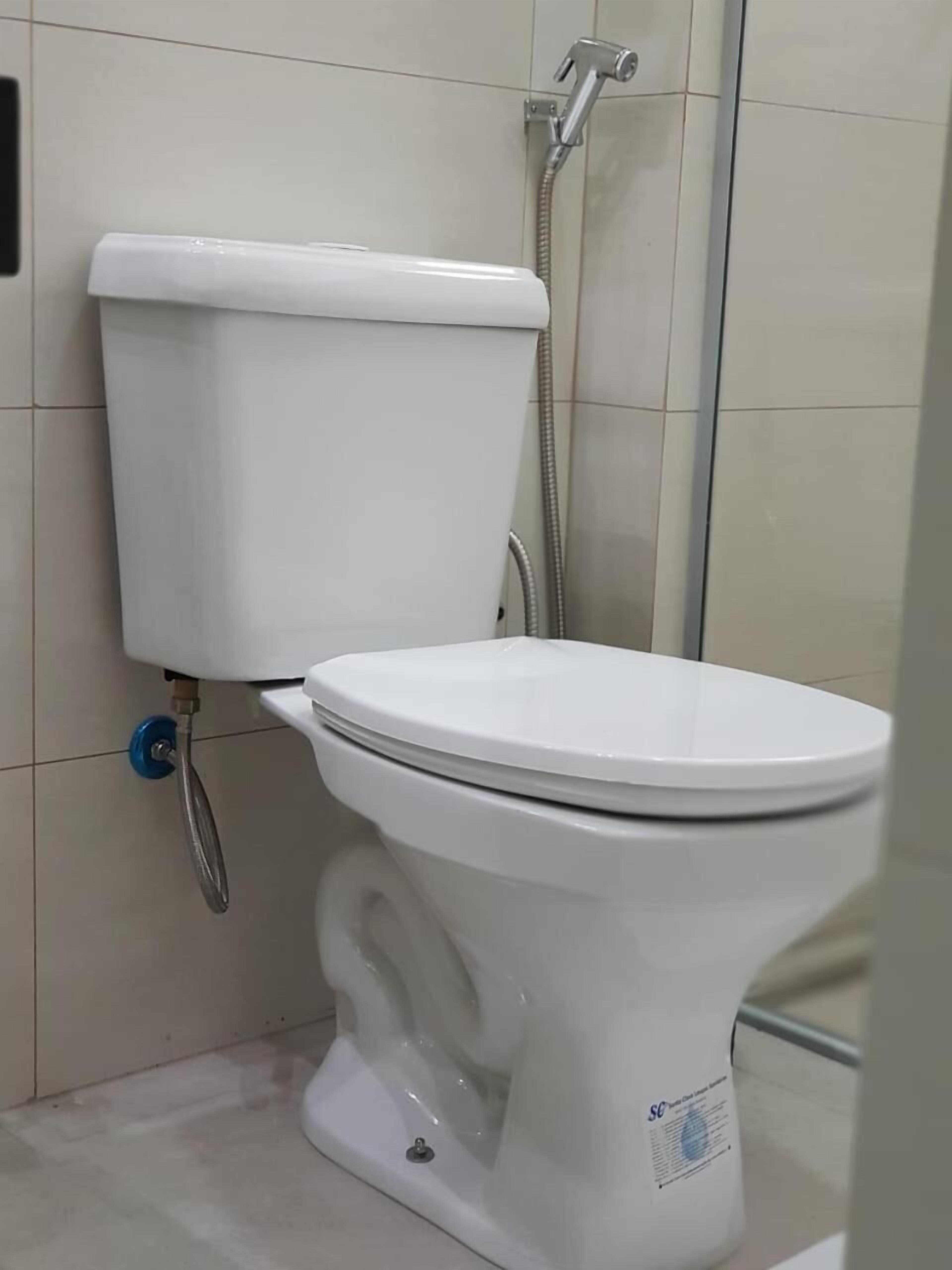 Inodoro blanco con descarga por pedal, bidé instalado en la pared y cabezal de ducha.