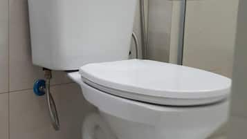Inodoro blanco con descarga por pedal, bidé instalado en la pared y cabezal de ducha.