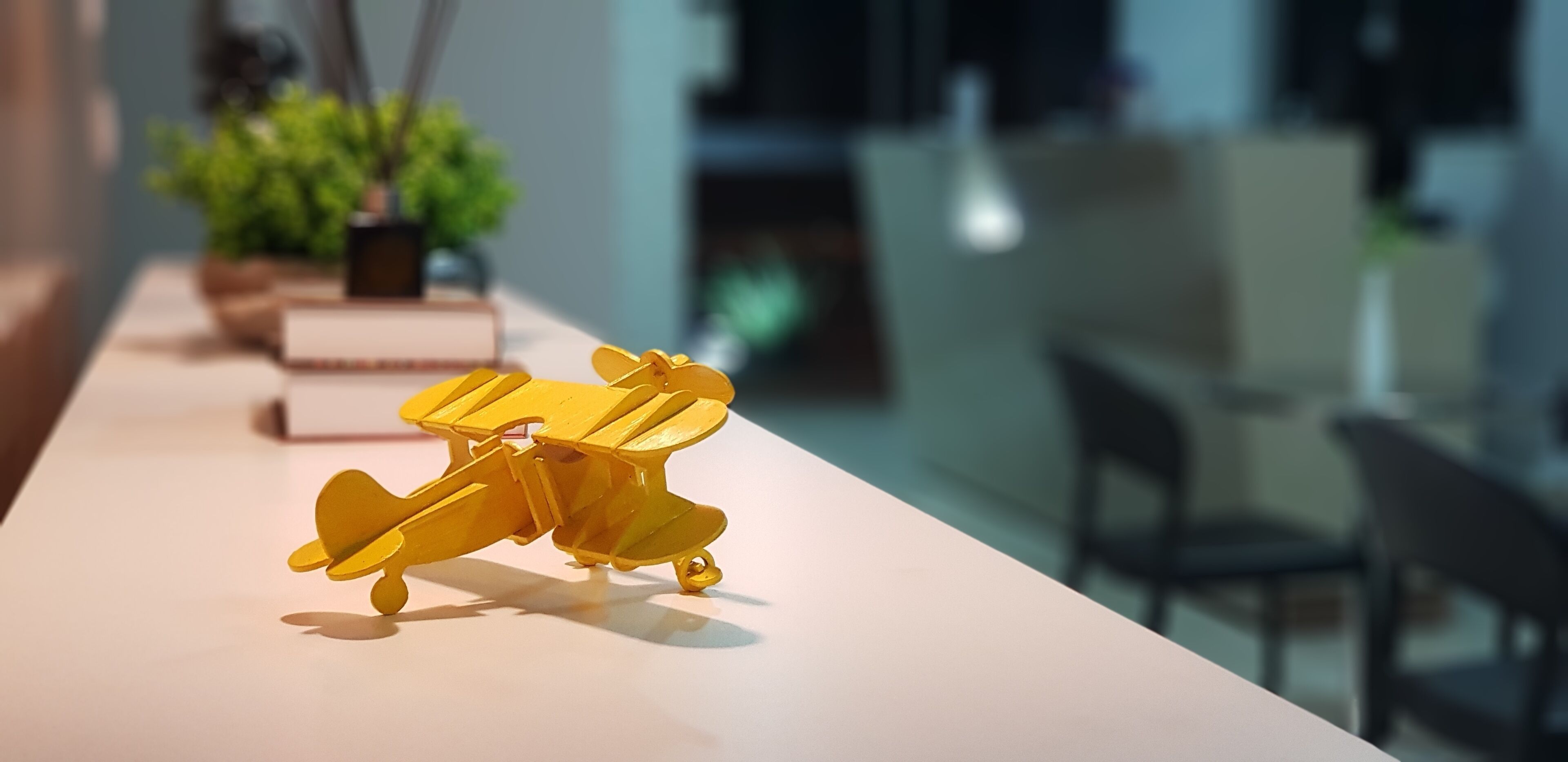 A model yellow airplane on a table in a room with a modern design, a potted plant, and a chair.