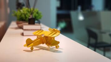 A model yellow airplane on a table in a room with a modern design, a potted plant, and a chair.