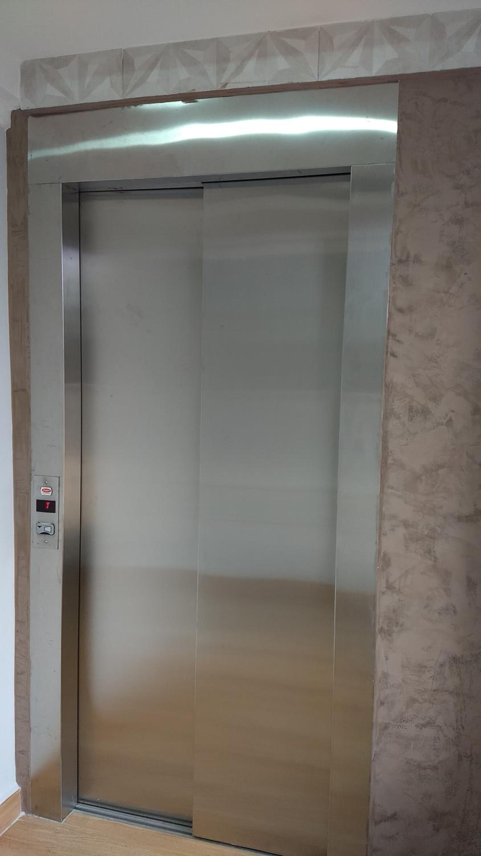 A metallic elevator with a control panel on the left side.
