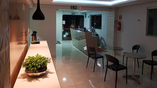 A modern hotel lobby with a reception desk, seating area, and a glass partition separating the lobby from the dining area. - Aero Inn Hotel (Uberlandia)