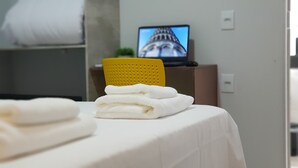 A neatly made bed with folded towels, a yellow chair, and a television displaying a building. - Aero Inn Hotel (Uberlandia)