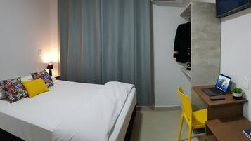 Una habitación de hotel con una cama, un escritorio con una computadora portátil, una silla y un equipo de aire acondicionado.