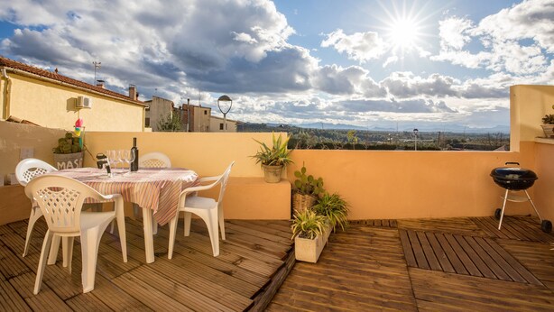 Un patio al aire libre con una mesa lista para comer, rodeado de plantas en macetas y una parrilla.