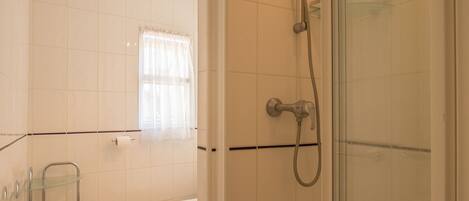 Un baño con ducha de mampara de vidrio, un inodoro y un estante de vidrio.