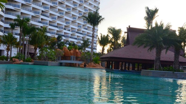 A swimming pool with a view of a high-rise hotel and palm trees. - Wyndham Garden Lingshui (Lingshui)