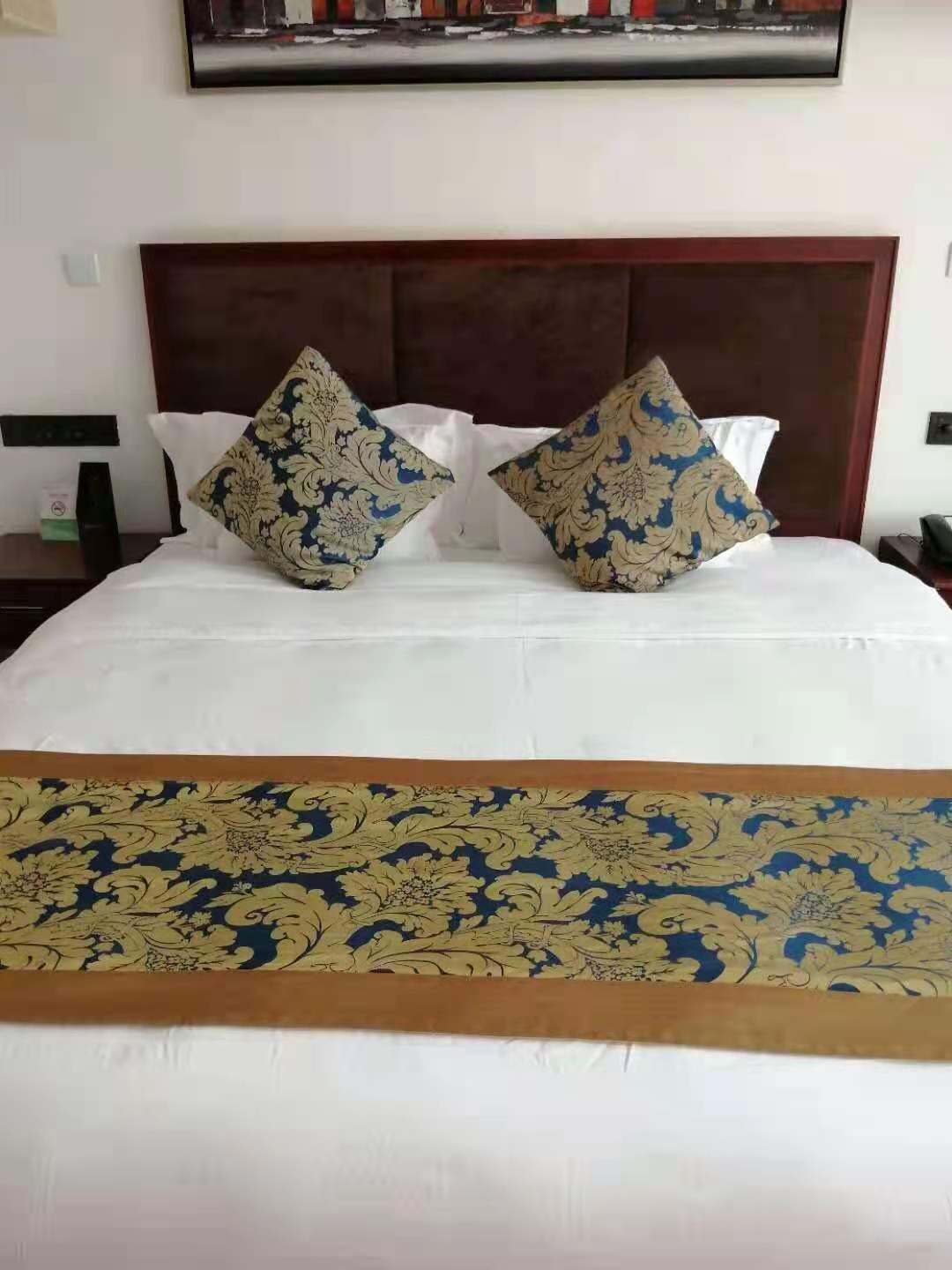 Un lit bien fait, avec une couette blanche et deux coussins décoratifs, une tête de lit en bois et un couvre-lit à motifs.