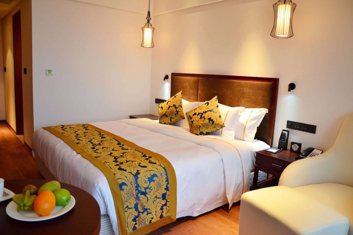 Ein Hotelzimmer mit einem großen Bett, Nachttischen, einem Sessel und einer Obstplatte auf einem kleinen Tisch.
