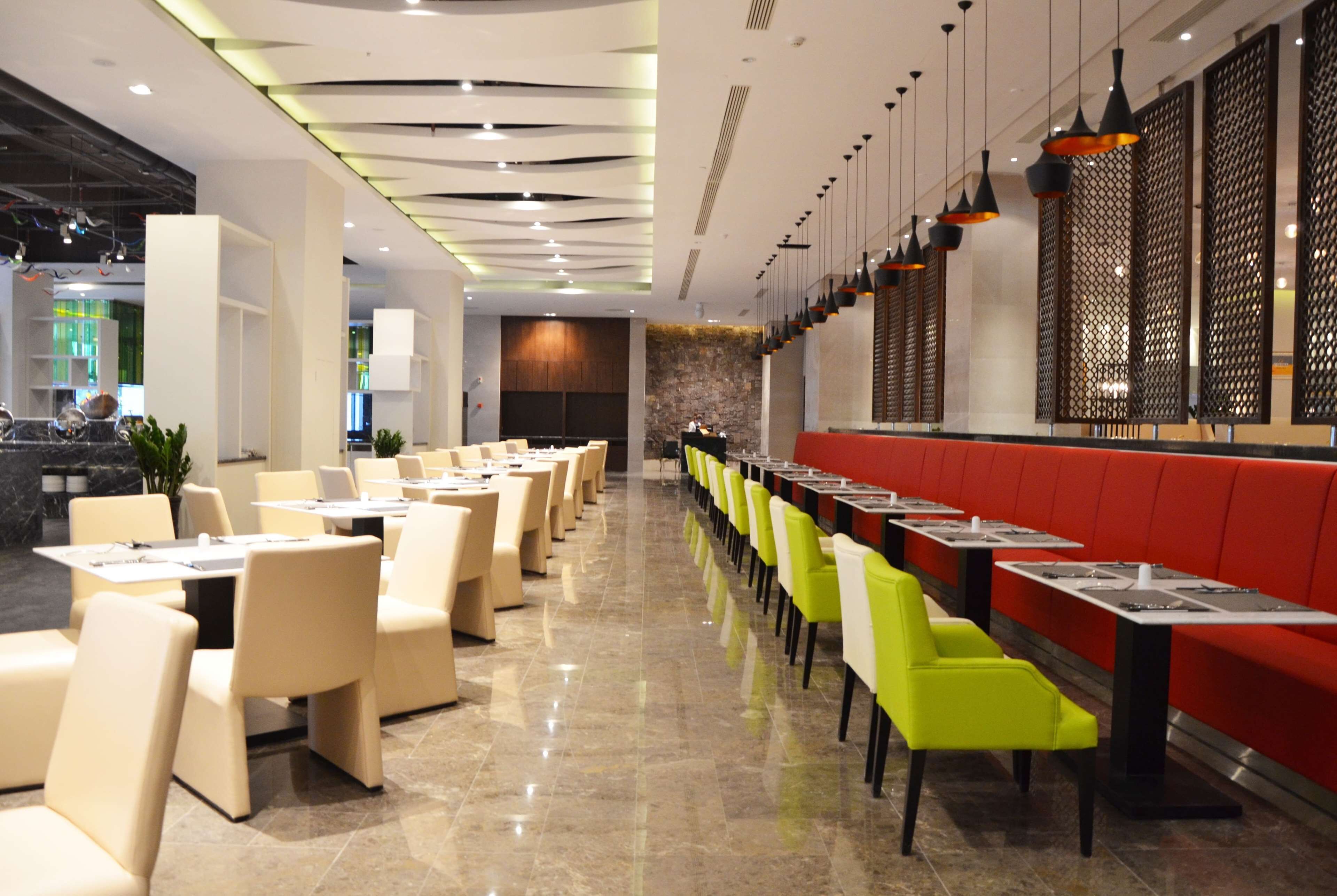 Ein modernes Restaurant mit Tischen und Stühlen, einer roten Sitzecke und dekorativer Beleuchtung.