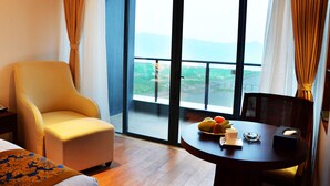 A hotel room with a large window, a round table with a fruit bowl, a chair, and a bed with a patterned bedspread. - Wyndham Garden Lingshui (Lingshui)