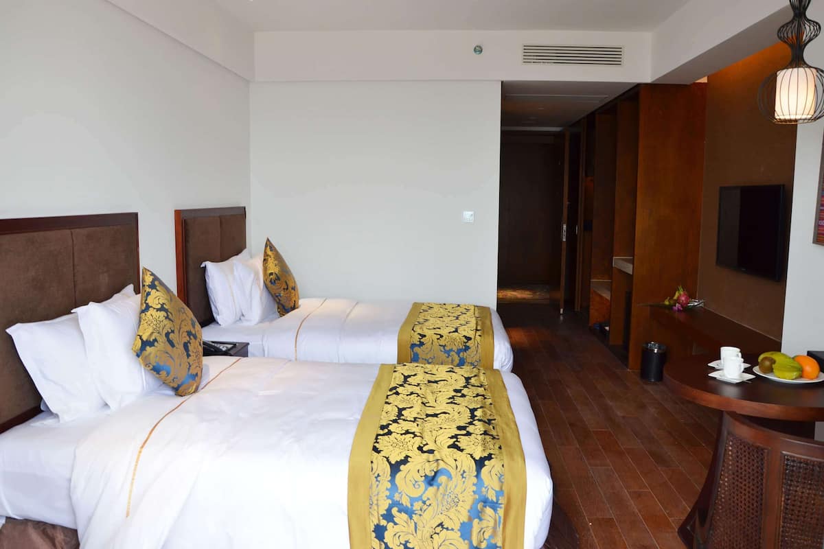 Ein Hotelzimmer mit zwei Betten, einem hölzernen Kopfteil, weißer Bettwäsche und einem dekorativen Laufschuh in Gold- und Blautönen.