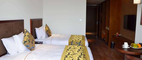 Quarto de hotel com duas camas, cabeceira de madeira, roupa de cama branca e um corredor de cama decorado em dourado e azul.