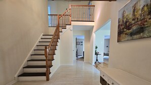 A spacious hallway with a wooden staircase leading to an upper level, a white console table, and a painting on the wall. - Lakefront/Legoland/West Point Retreat Under 1 Hour From NYC! Heated pool & Spa! (Monroe)