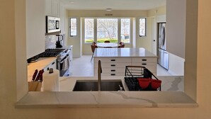 A modern kitchen with white cabinets, a central island, and a dining area with a table and chairs. - Lakefront/Legoland/West Point Retreat Under 1 Hour From NYC! Heated pool & Spa! (Monroe)