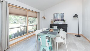 En spiseplads med et bord, stole, et sort skab, et billede og en gulvlampe.