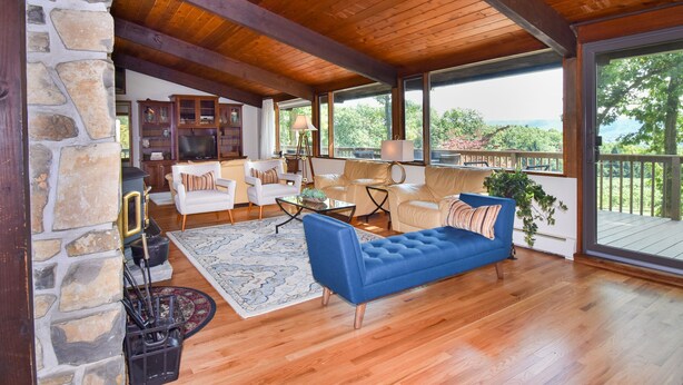 A spacious living area with a stone wall, wooden ceiling, and large windows offering a view of the outdoors.