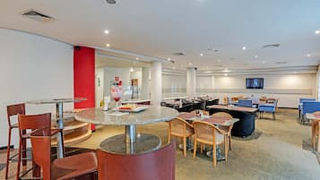 Um lobby de hotel moderno com mesas redondas, cadeiras de couro e um bar.