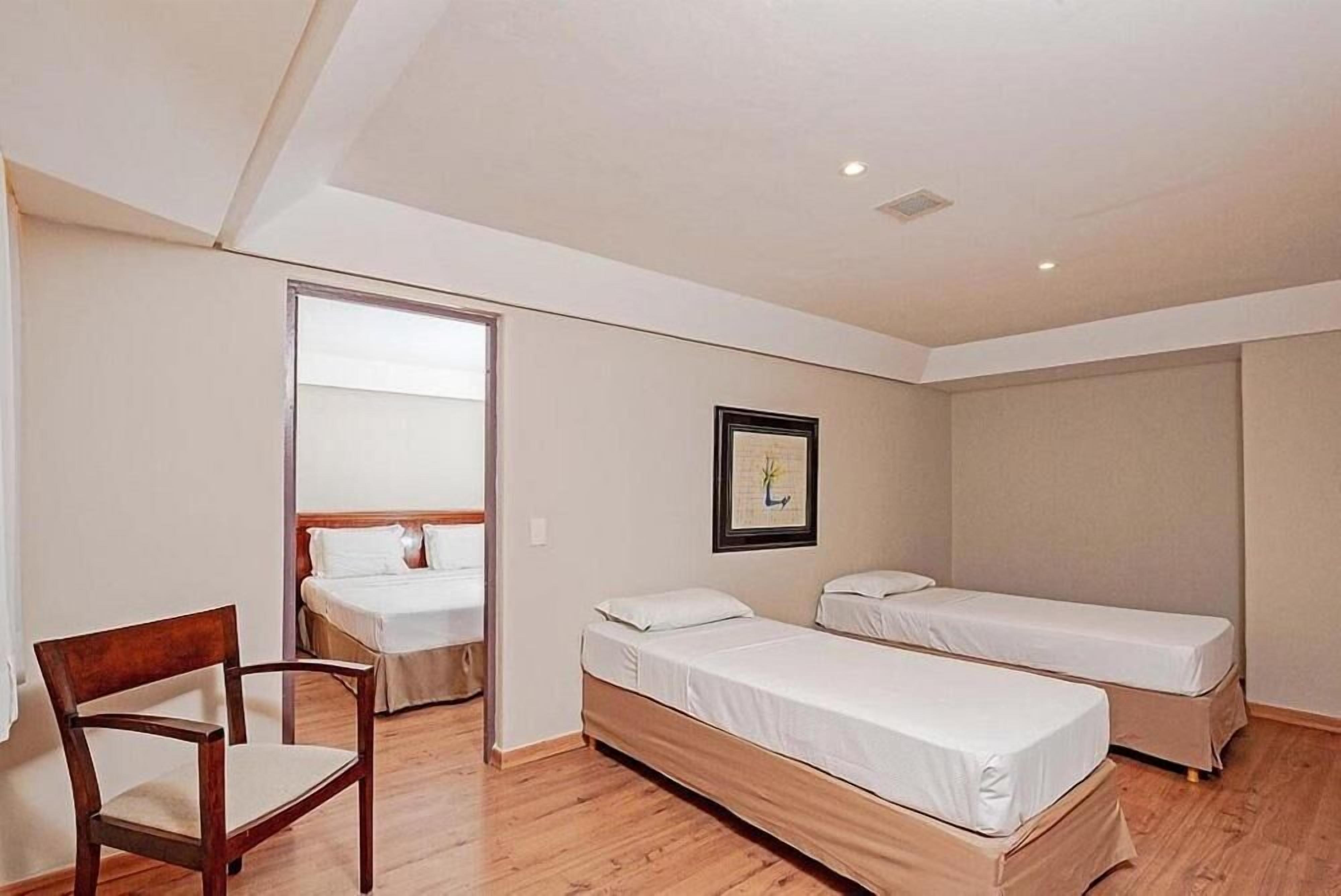 Una habitación con dos camas individuales, una silla de madera y un cuadro en la pared.