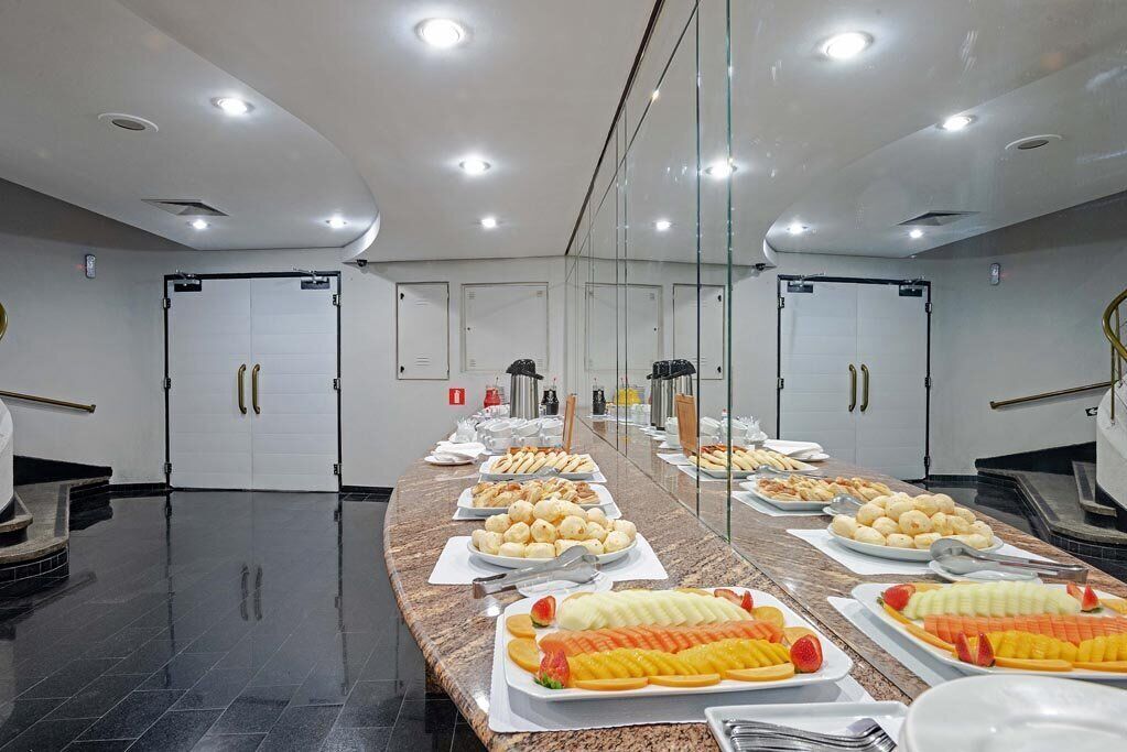 A buffet setup with various food items and utensils on a long counter, with doors and a fire extinguisher in the background.