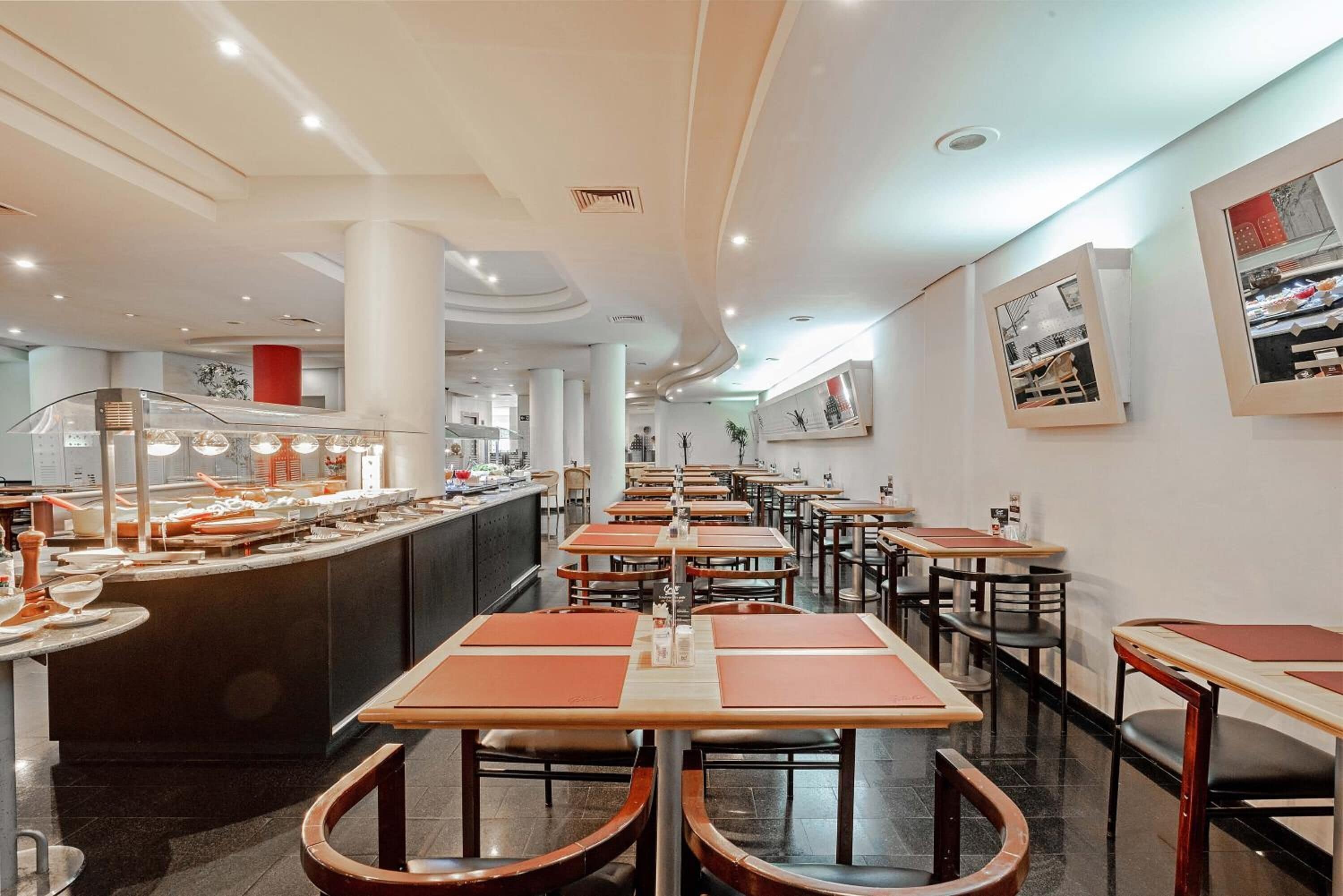 Un interior de restaurante moderno con mesas largas, una barra central y un ambiente limpio e iluminado.