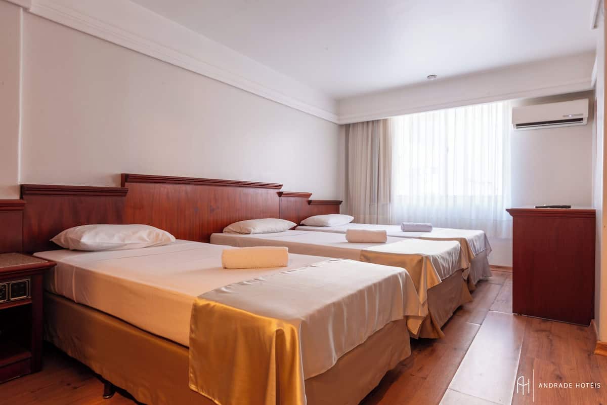 A hotel room with three beds, wooden headboards, and a wooden desk.