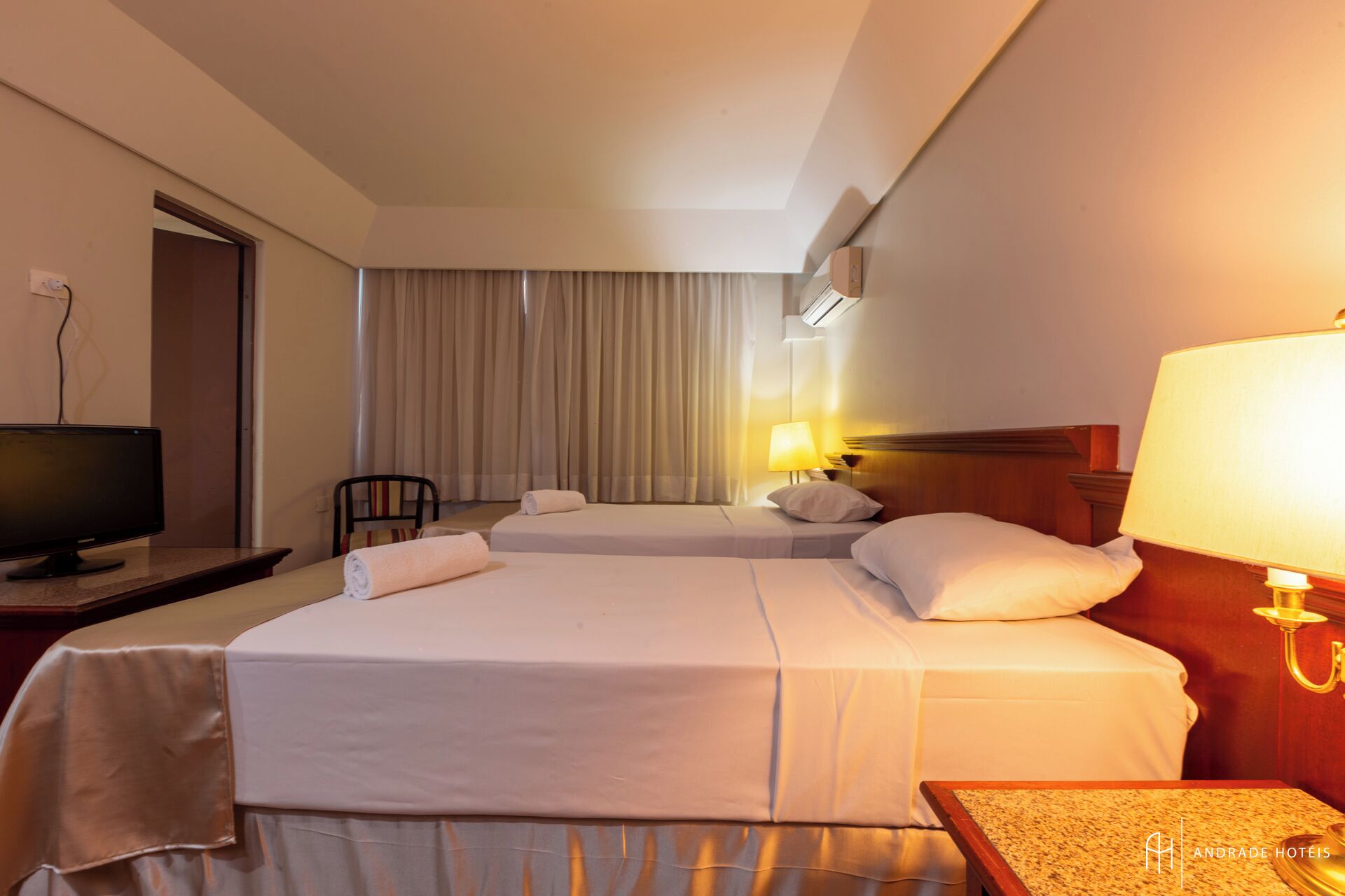A hotel room with two beds, a television, a desk, a chair, and a lamp.
