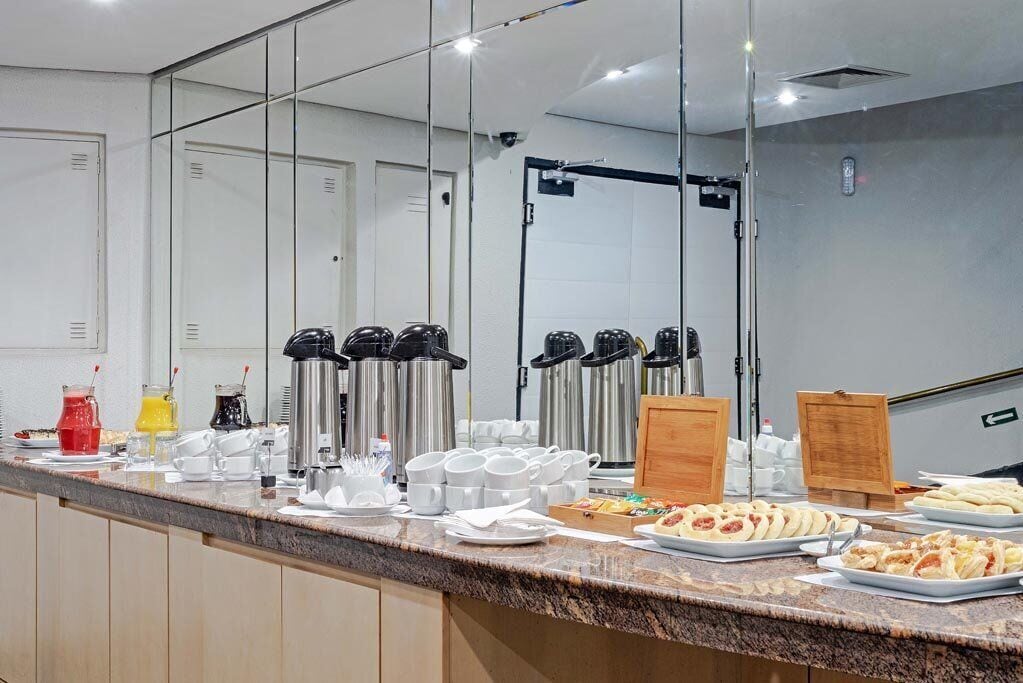 Disposição de buffet de café da manhã com máquinas de café, xícaras e diversas opções de alimentos.