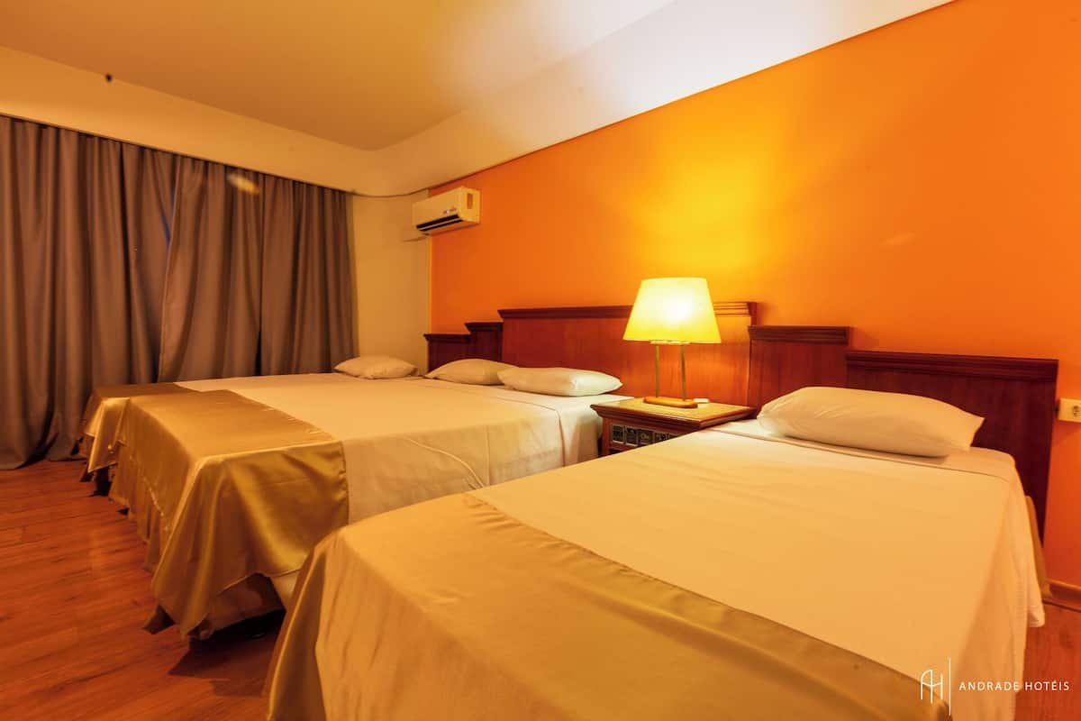 A hotel room with two single beds, a wooden floor, an air conditioning unit, and a lamp on a bedside table.