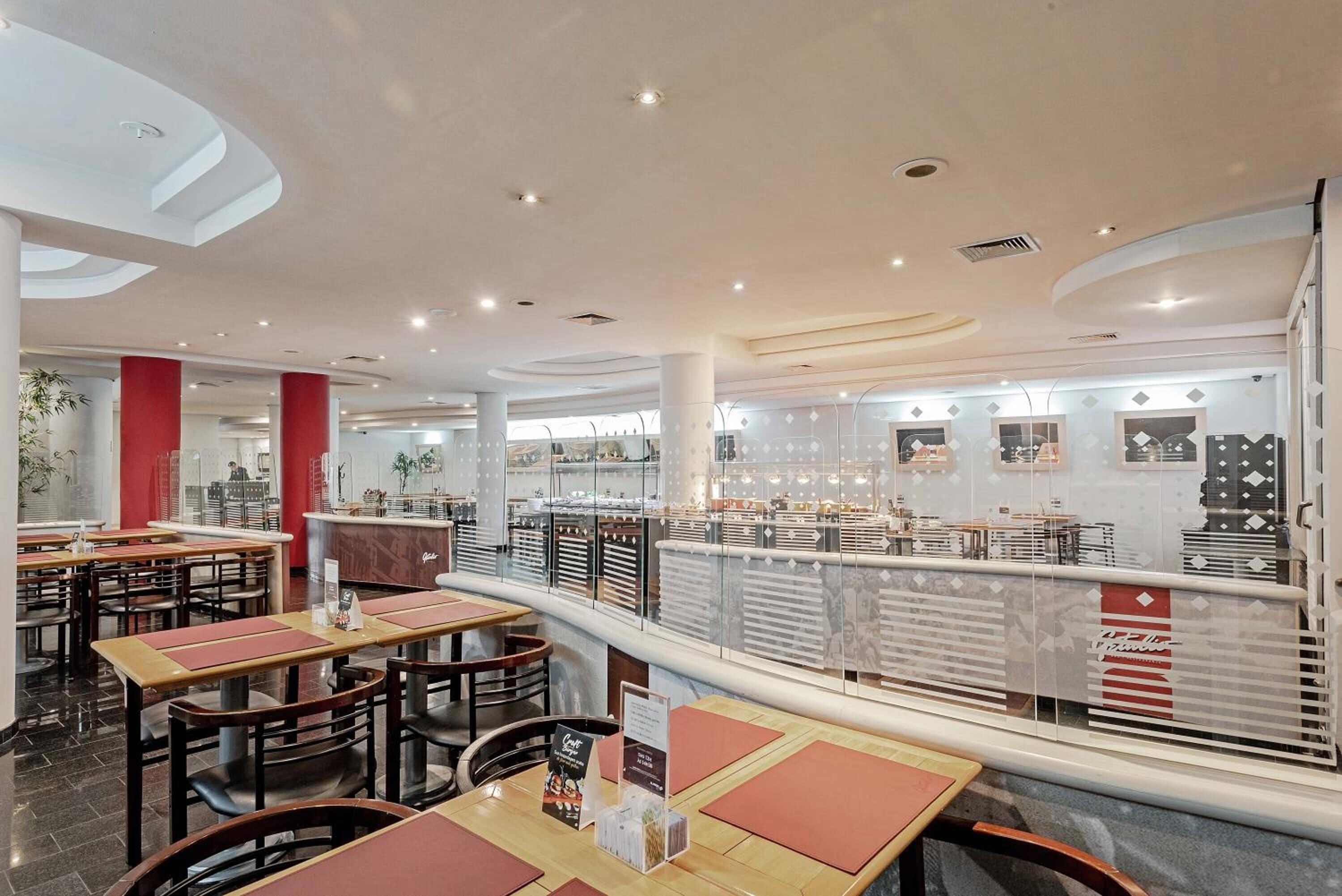 Um interior de restaurante moderno com várias mesas e cadeiras, um balcão com menu e uma parede decorativa com padrões geométricos.