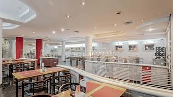 Um interior de restaurante moderno com várias mesas e cadeiras, um balcão com menu e uma parede decorativa com padrões geométricos.