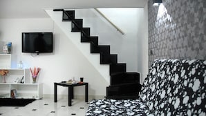 Una sala de estar moderna con una escalera negra, un televisor de pantalla plana, una mesa de centro negra y un sofá estampado.