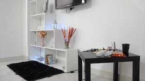 Una sala de estar moderna con un televisor negro en la pared, un estante blanco con objetos decorativos, una mesa de centro negra y una alfombra negra.