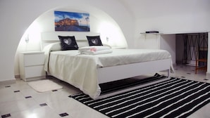 Un dormitorio moderno con una cama blanca, dos almohadas con forma de corazón, una mesita de noche, un cuadro de un paisaje urbano y una alfombra a rayas negras y blancas.