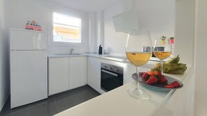 Ett modernt kök med vita skåp, en inbyggd ugn och ett fönster. På köksbänken står två glas vitt vin.
