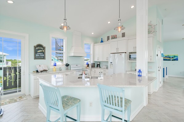 A modern kitchen with white cabinets, a large island, and blue chairs.