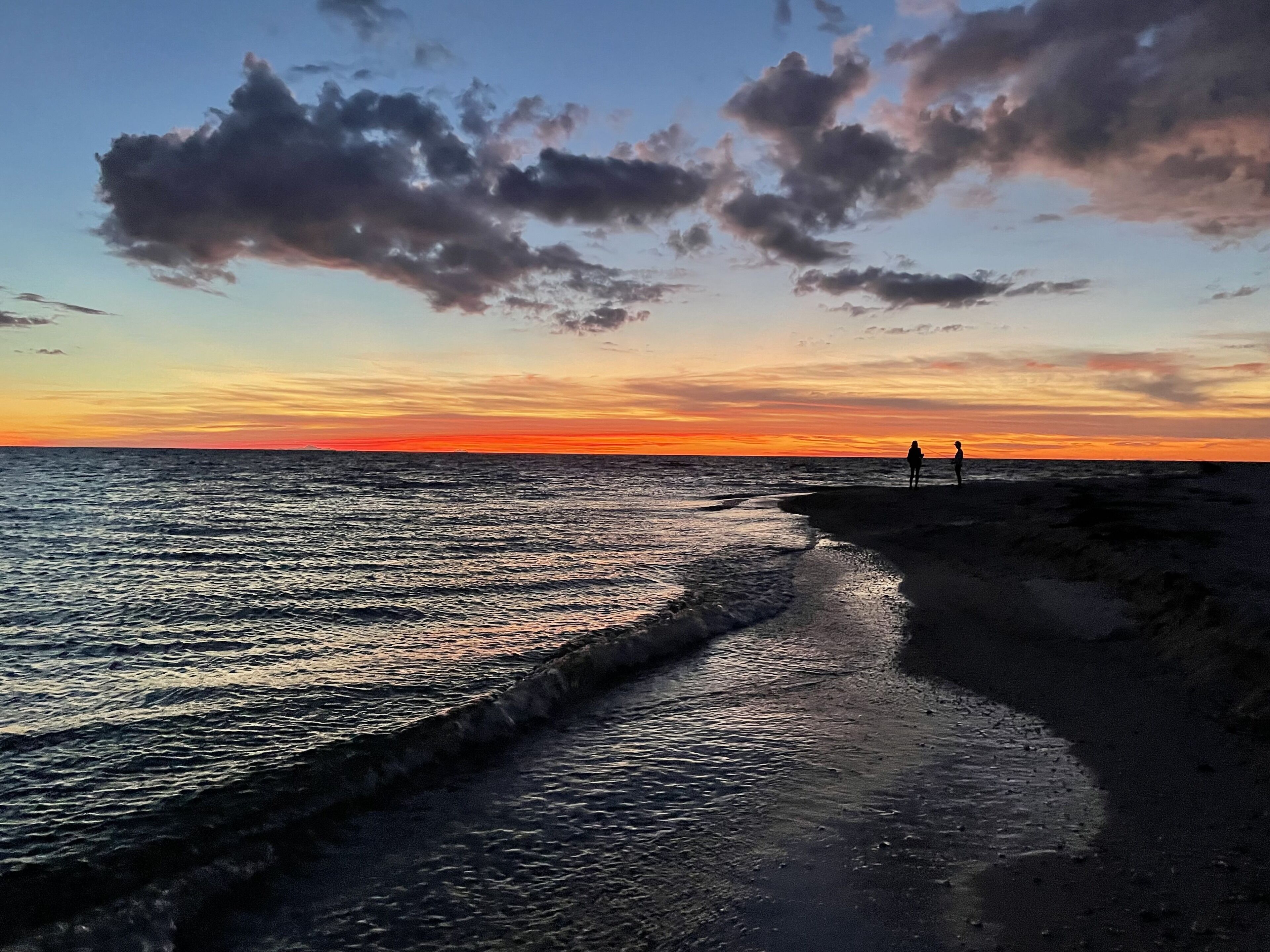 A beach at sunset with two people standing on the shore.