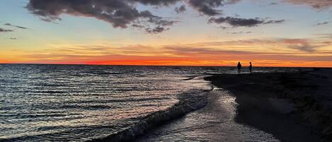A beach at sunset with two people standing on the shore.