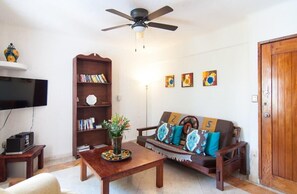 A living room with a ceiling fan, a sofa with patterned cushions, a bookshelf, and a television on a stand.