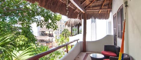 A balcony with a thatched roof, wicker furniture, and a view of a residential area.