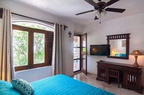 A bedroom with a bed, a ceiling fan, a TV mounted on the wall, and a window with curtains.
