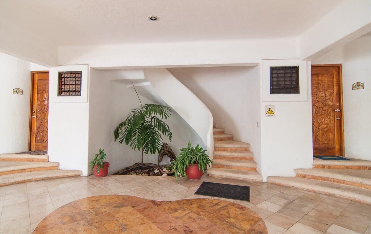 A lobby with a curved staircase, potted plants, and a tiled floor.