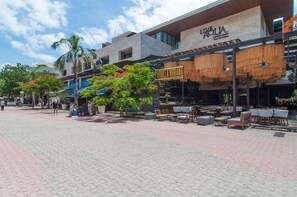 A modern outdoor seating area with tables and chairs, a palm tree, and a building with a sign reading "LIVE AQUA".