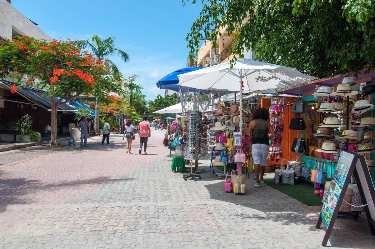 A pedestrian street with outdoor market stalls selling hats and bags.