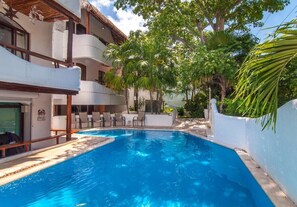 A swimming pool with lounge chairs and a building with balconies.